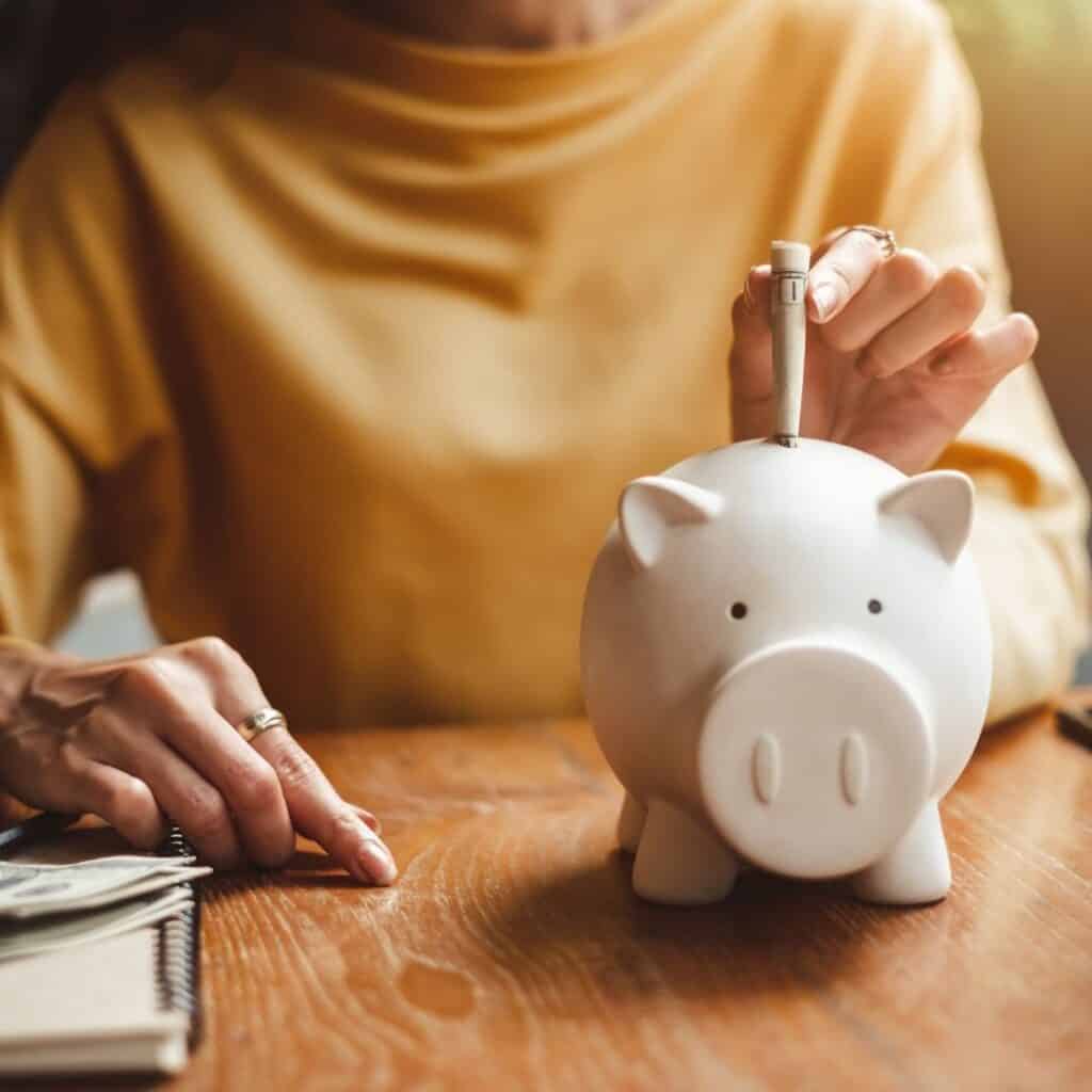 Easiest ways to save that are pain free, smart, simple and sensible.  image of a piggy bank with woman placing in money