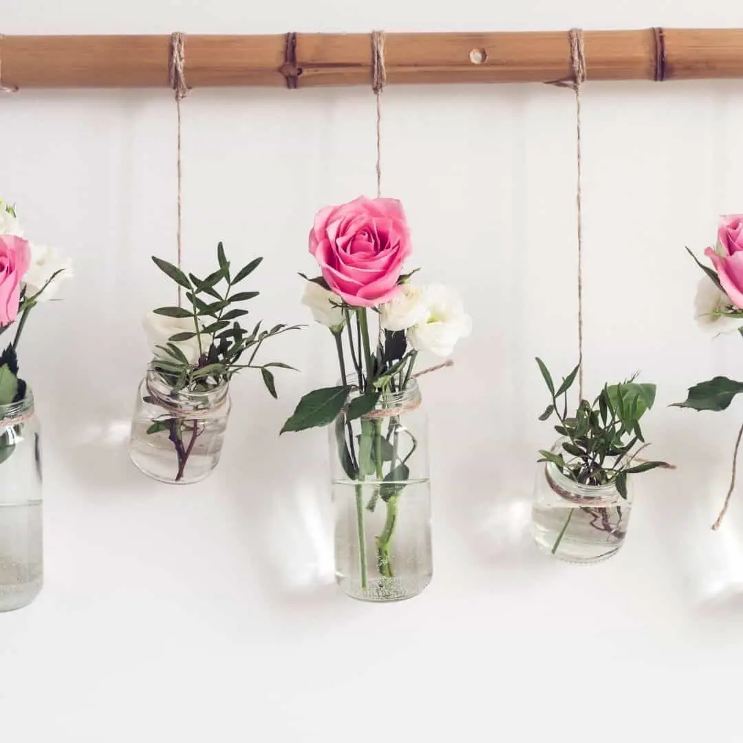 affordable upcycle ideas; image of glass jars repurposed as hanging vases with pink roses and greenery