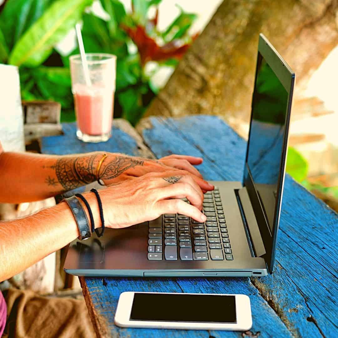 digital nomad; image of laptop on bench outdoors tropical tree in background