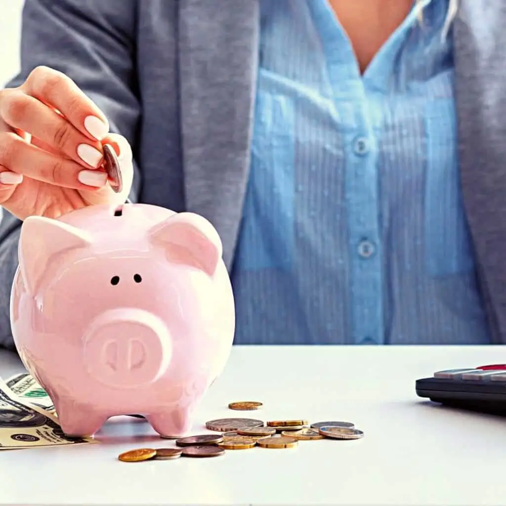 savings and budgeting tips; image of woman placing coins in a pink piggy bank